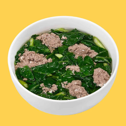 White bowl of clear broth soup with green leafy vegetables and chunks of minced crab meat on yellow background