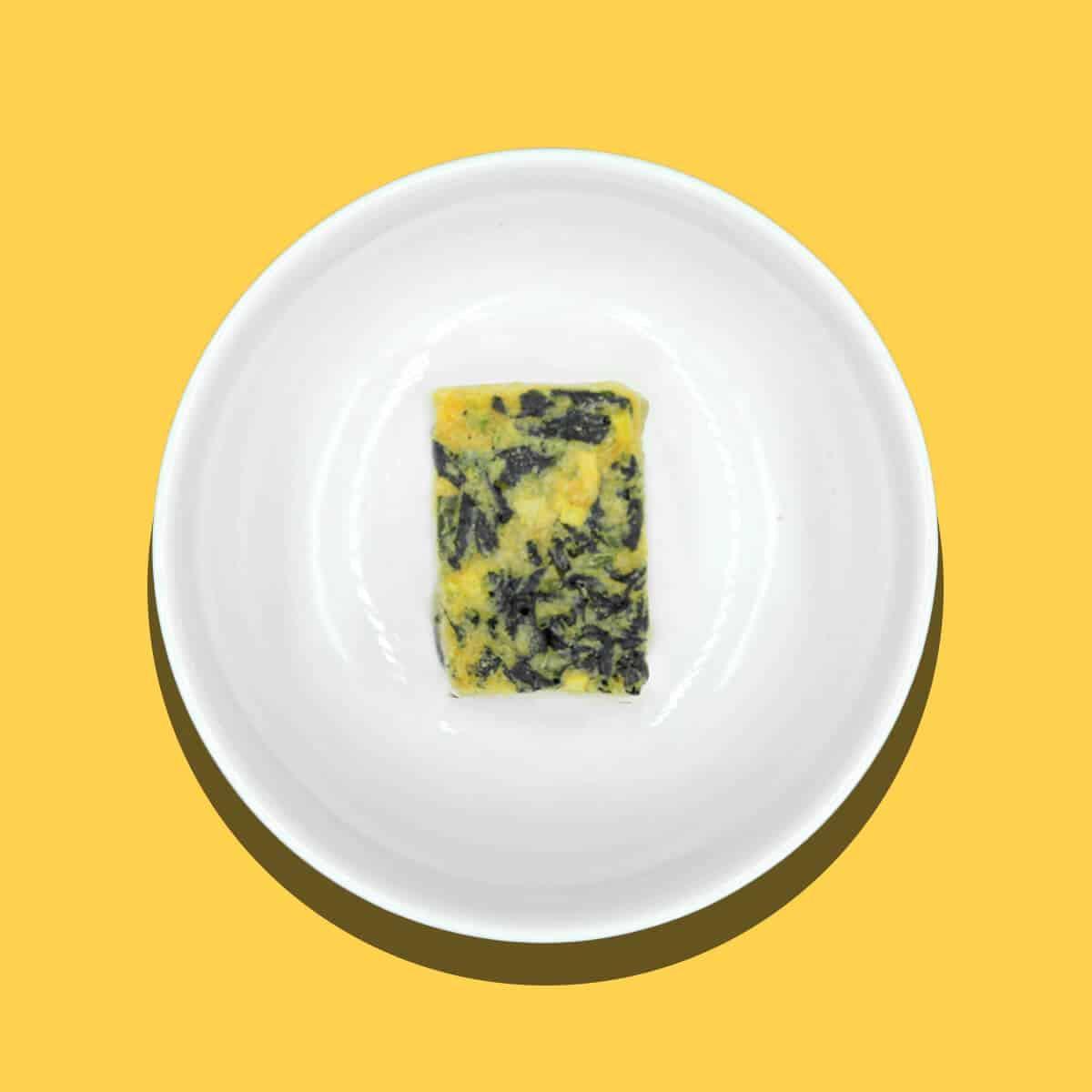 Small rectangular miso block with seaweed on a white plate against yellow background