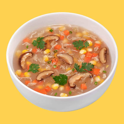White bowl of shiitake mushroom soup with corn, carrots, cilantro, and herbs on yellow background