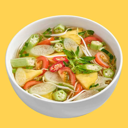 white bowl of vegan vegetable soup with okra, tomato, pineapple, chili, and greens on yellow background